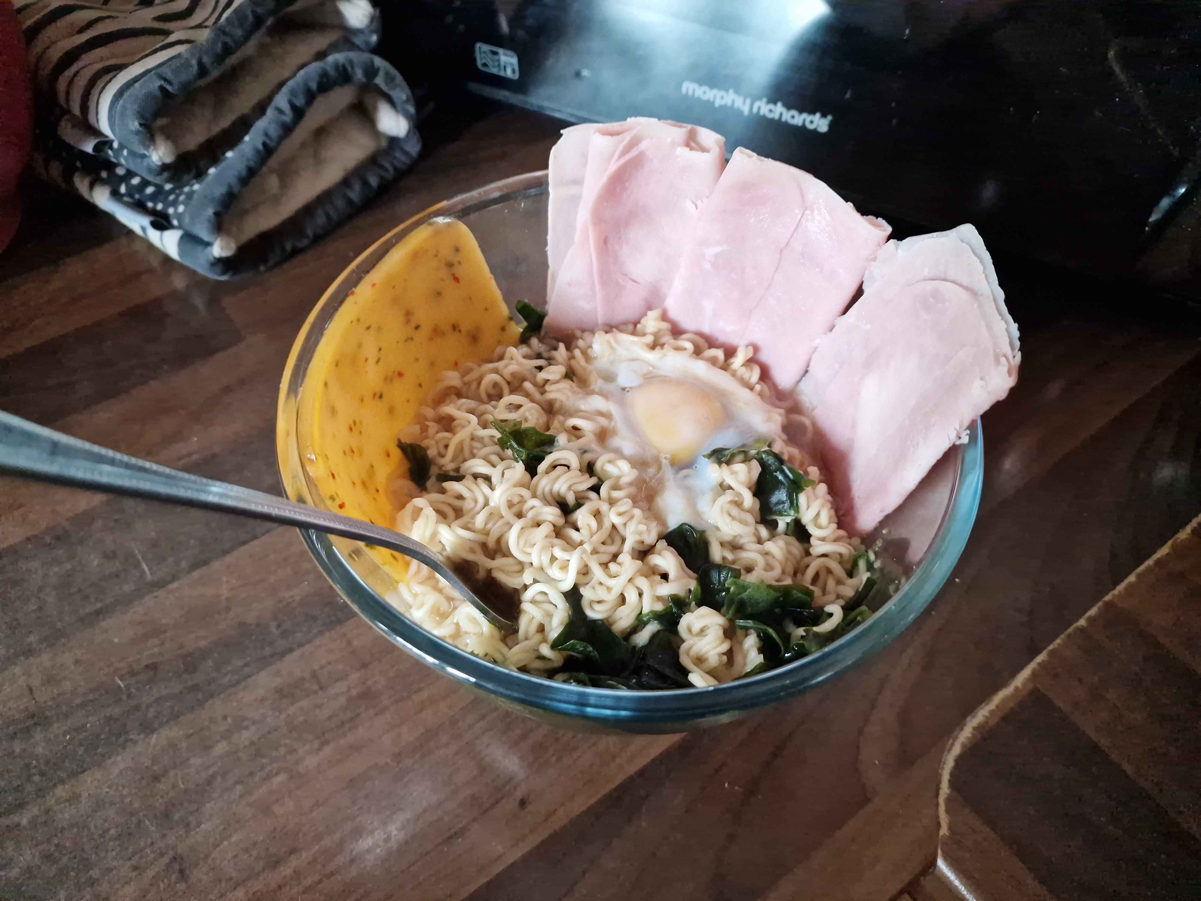 The prepared bowl of noodles with slices of ham and cheese around the sides, and an egg in the middle.