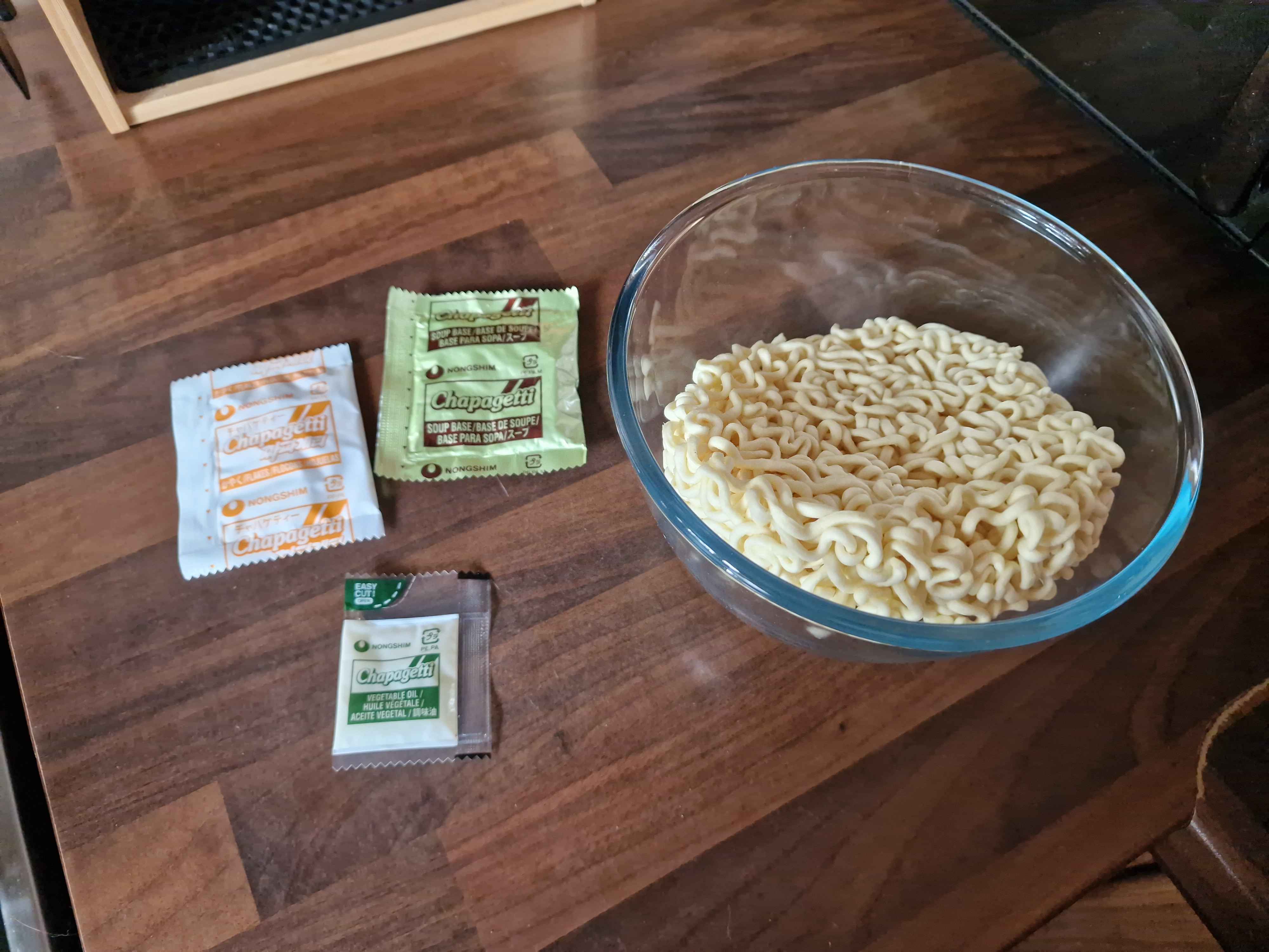 The contents of the package laid out, with three packets and a large round block of noodles in a glass bowl.