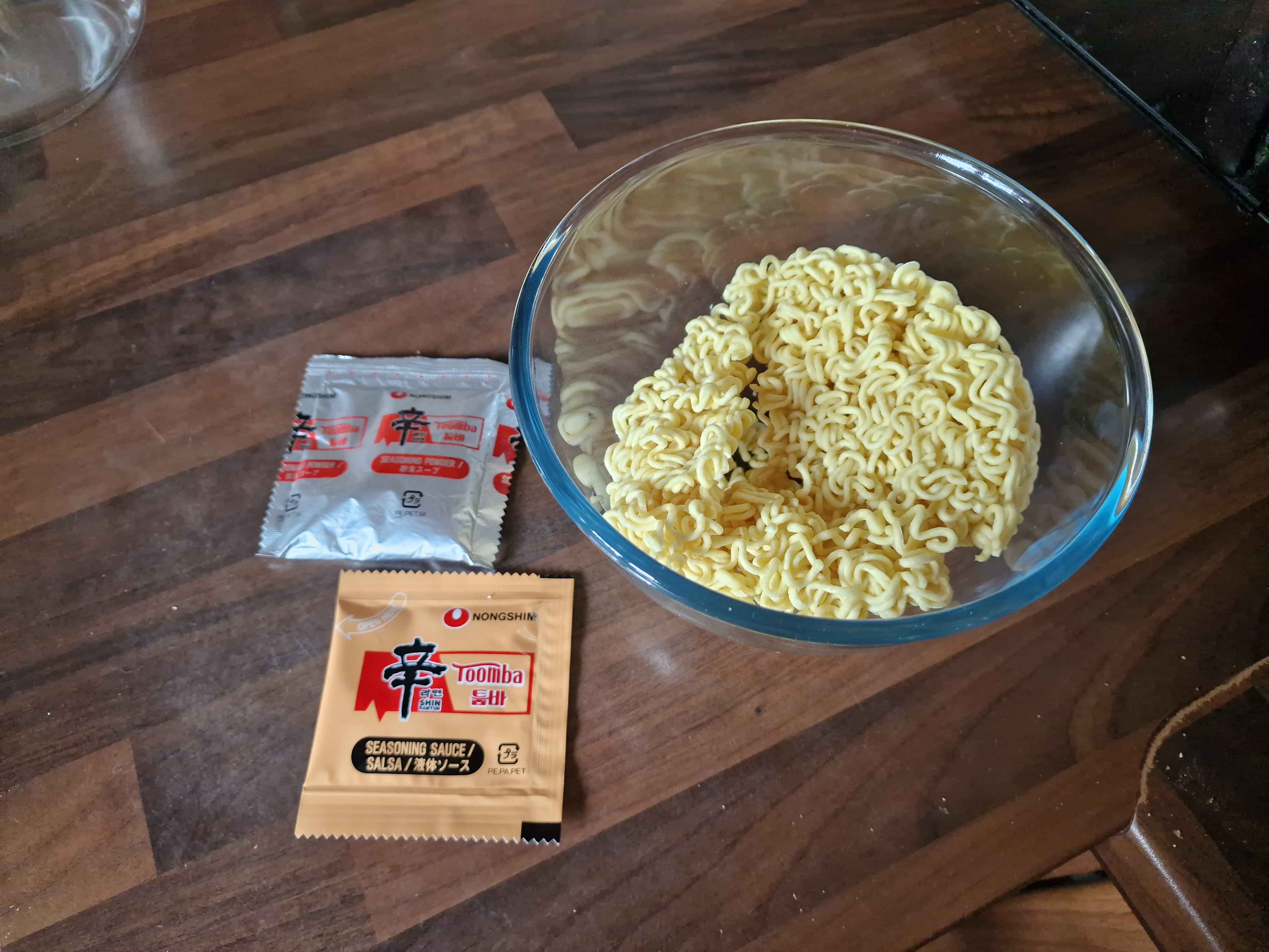 The bare noodles in a bowl, next to the two flavour packets containing powder and sauce.