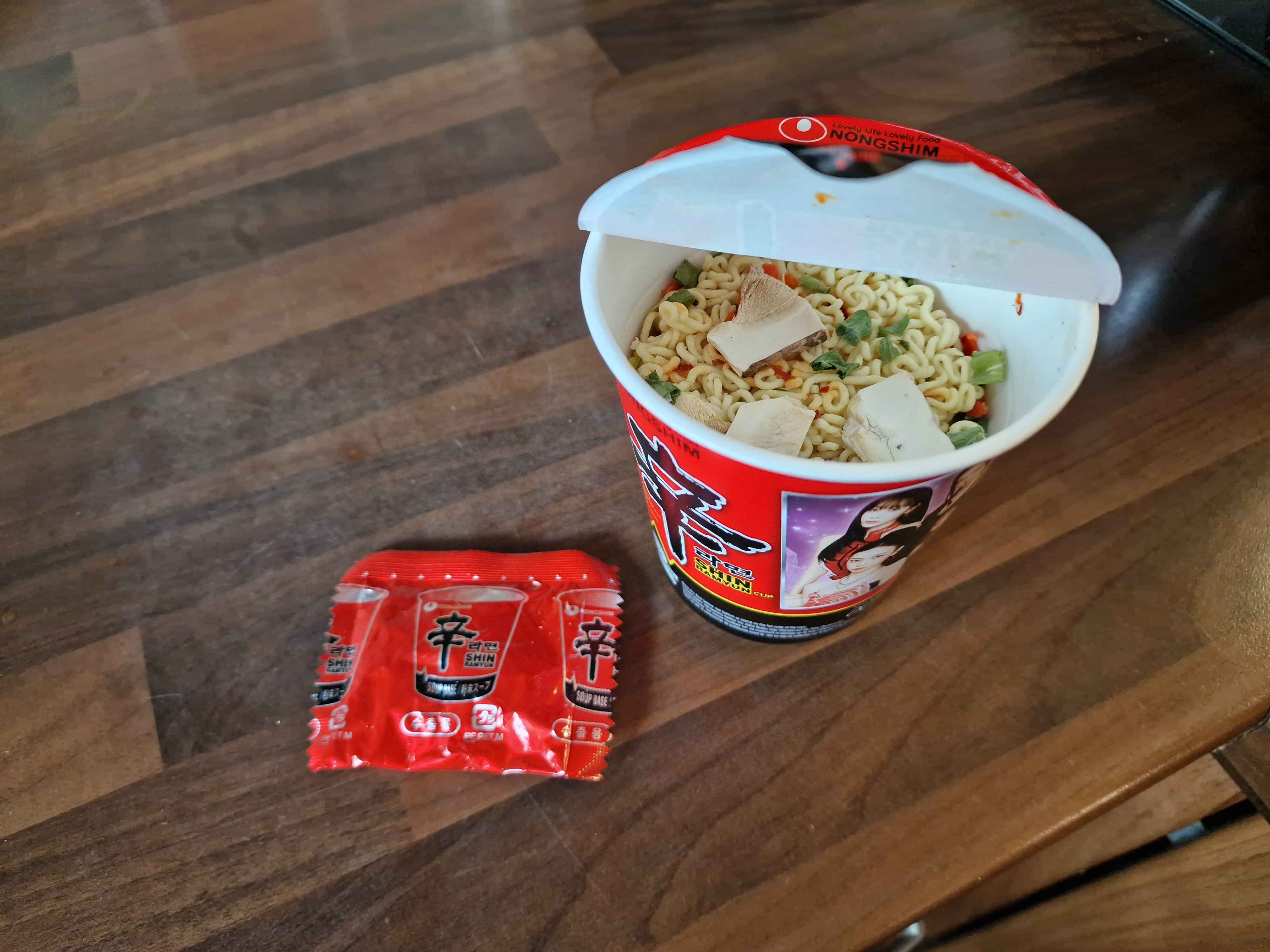 The Shin Ramyun cup, unprepared and open, with a powder sachet next to it.