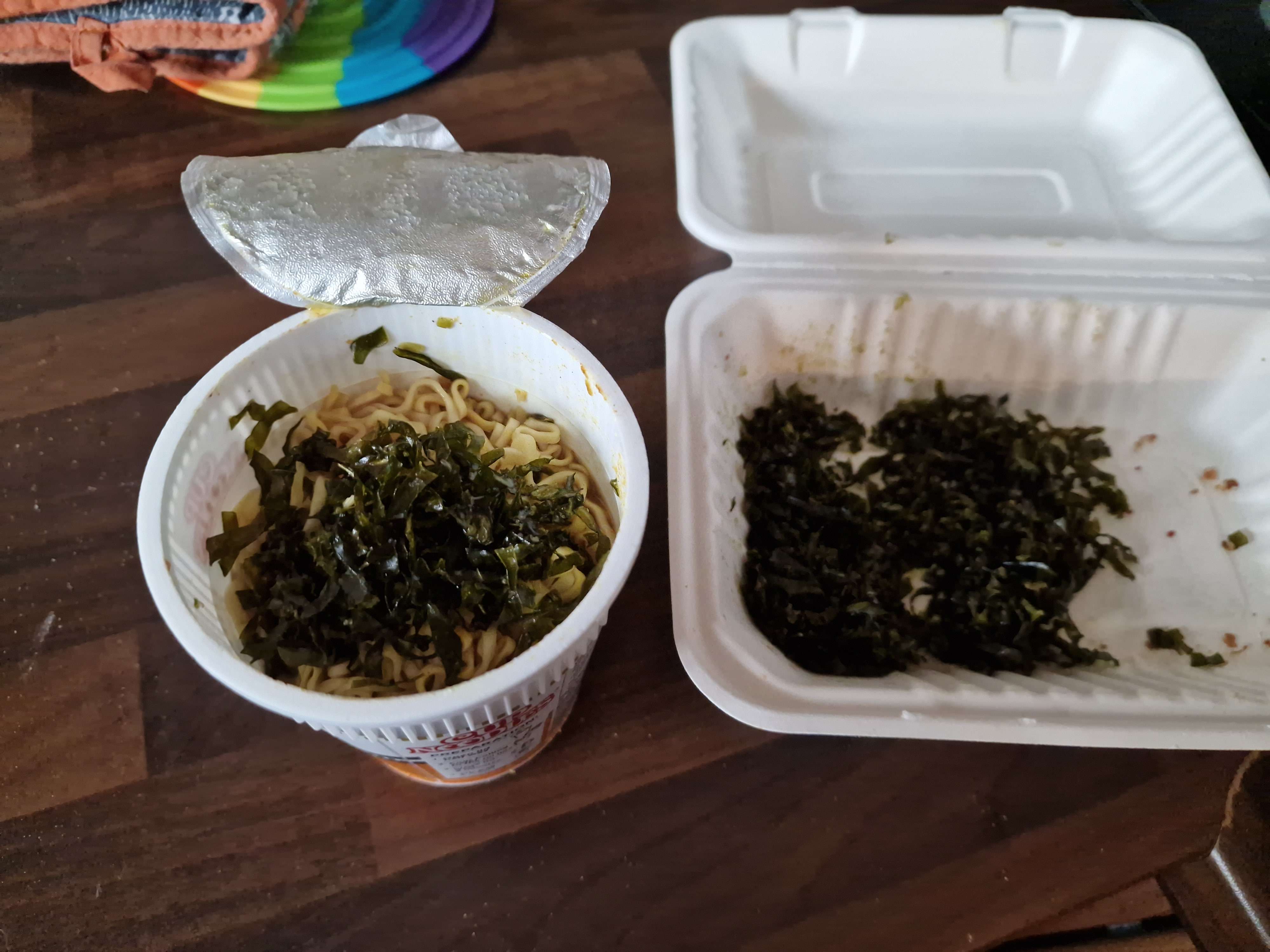 Prepared cup noodle with crispy seaweed, next to takeout container